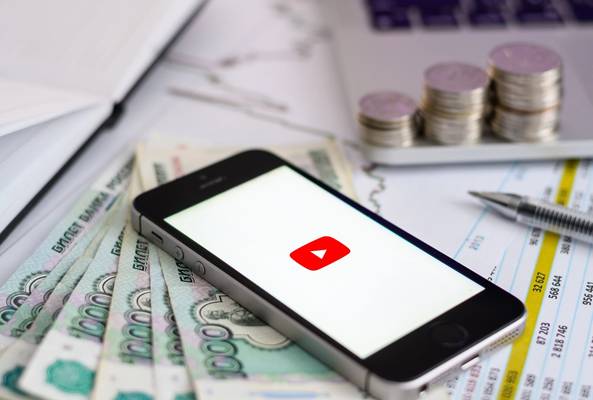 Smartphone with YouTube logo on screen, Russian rubles, coins, and financial documents.