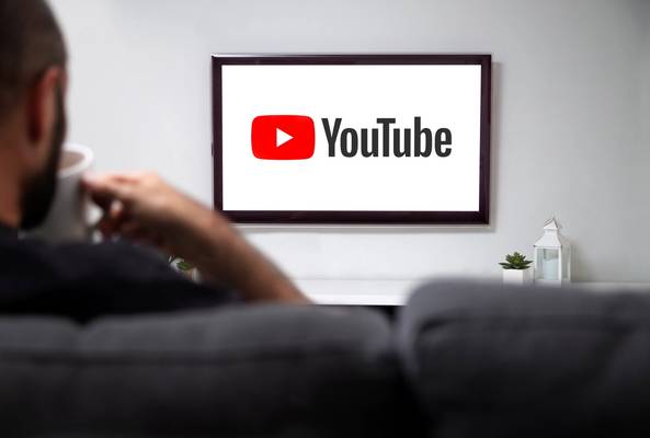 Person watching YouTube logo on TV screen while holding a cup on a gray couch.