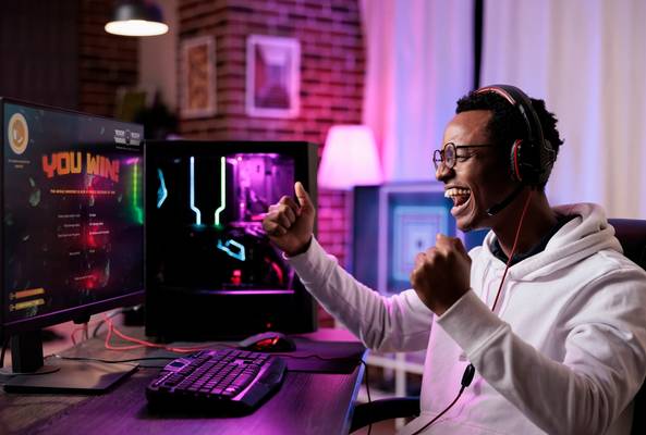 Excited gamer celebrating victory while playing video games on a desktop computer setup.