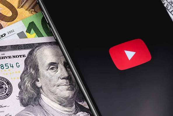 Smartphone showing YouTube logo on screen placed on mixed US and Euro currency bills.