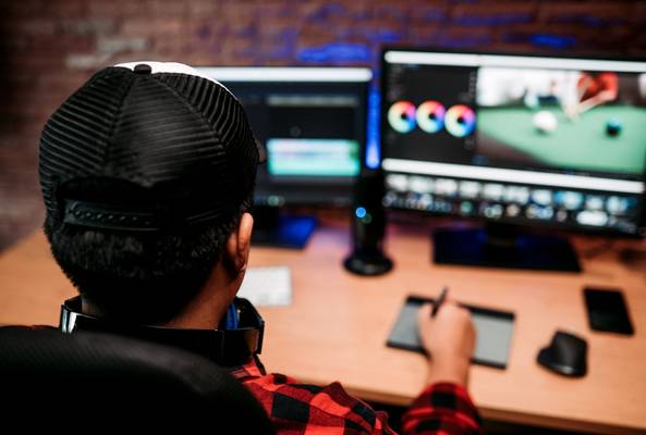 Video editor working on color grading using graphics tablet and dual monitors at desk