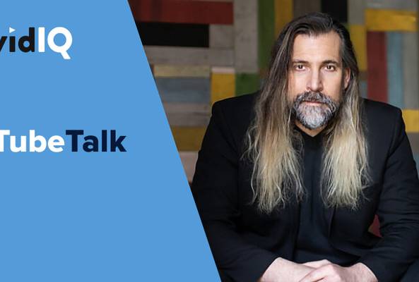 Man with long hair and beard sitting beside vidIQ TubeTalk logo on blue background
