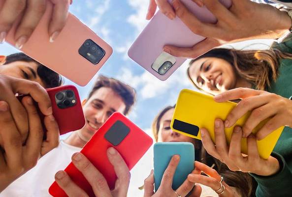 Group of diverse people holding smartphones in colorful cases outdoors with blue sky