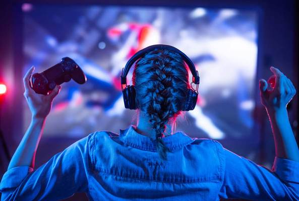 Gamer with braided hair wearing headphones celebrating victory while holding controller indoors
