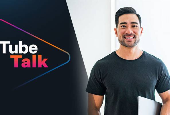 Smiling man with laptop standing next to Tube Talk logo on dark and white background.