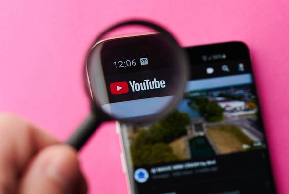 Magnified YouTube logo on smartphone screen with pink background and video thumbnail visible