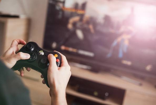 Person holding black Xbox controller playing video game on TV screen at home
