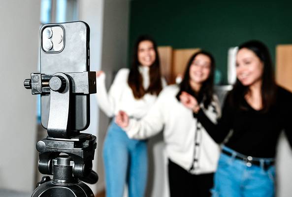 Smartphone mounted on tripod recording three women posing in casual clothing indoors