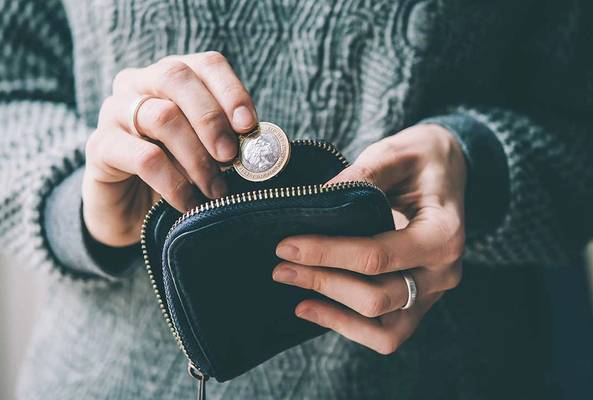 Person holding a coin above a small black wallet, wearing a gray knitted sweater.