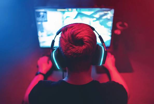 Gamer wearing headphones playing video games on a glowing computer screen in dark room