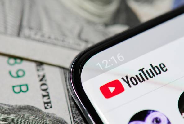 Close-up of YouTube app on smartphone screen with US dollar bills background.
