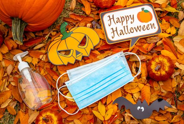 Halloween decorations with face mask, hand sanitizer, pumpkins, and autumn leaves.