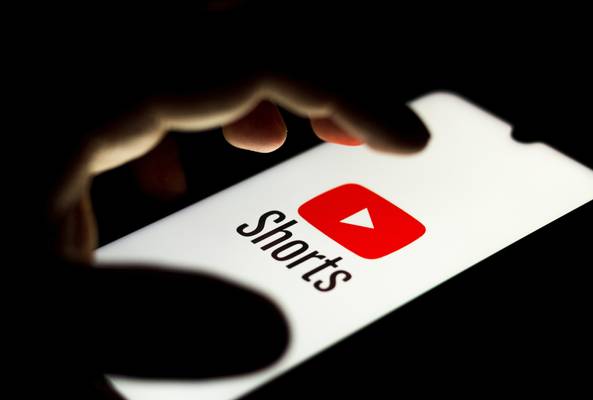 Close-up of hand holding phone with YouTube Shorts logo on screen in dark setting