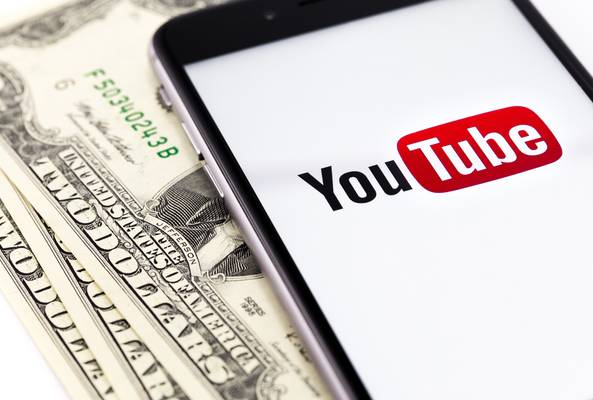 Smartphone displaying YouTube logo on screen placed on US dollar bills background.