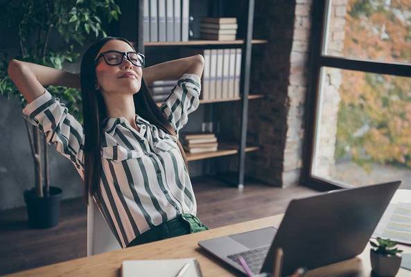 Woman relaxing at desk in modern office with laptop and books, enjoying break