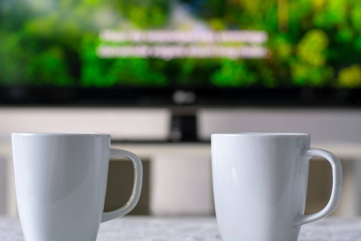 Two coffee cups sitting on a table and a TV showing media captions