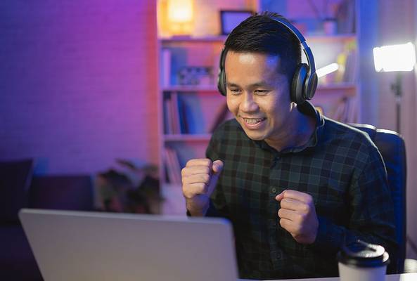 Man wearing headphones celebrating success while working on laptop at home desk