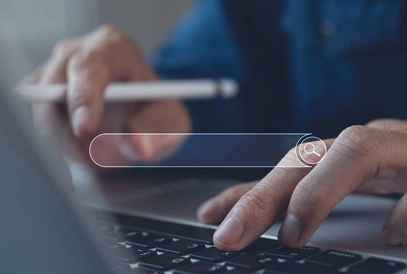 Person using laptop keyboard with search bar overlay and digital pen in hand
