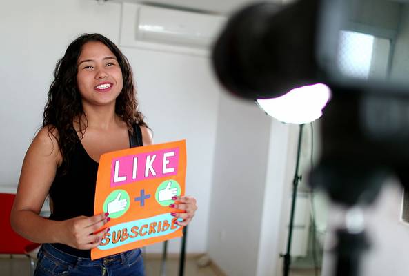 Young woman recording video holding a sign that says Like and Subscribe for channel growth