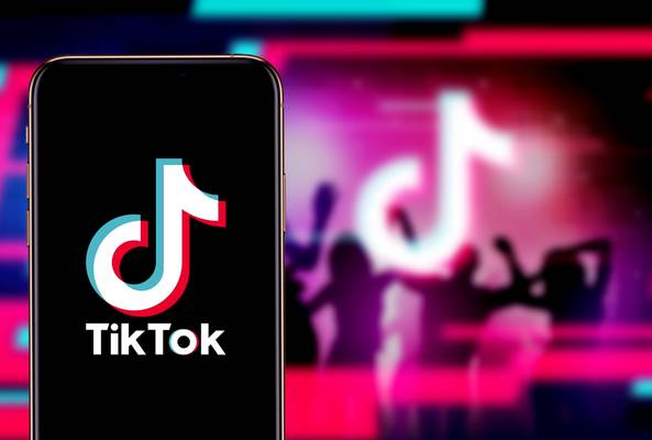 Smartphone displaying TikTok app logo with blurred dancing crowd background in neon colors