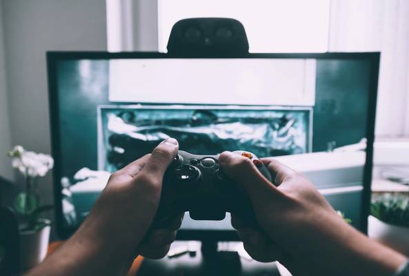 Person holding a black gaming controller playing a video game on a TV screen at home.