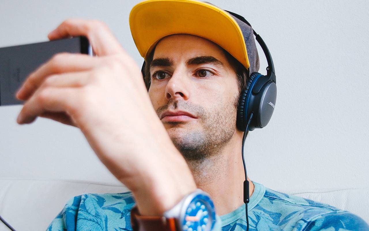 Man in yellow cap wearing headphones and holding a smartphone for a selfie or video call
