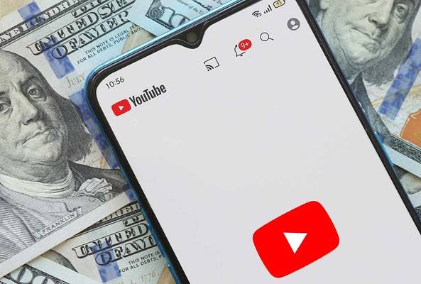 Smartphone showing YouTube app on screen over US hundred-dollar bills background