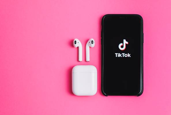 Smartphone showing TikTok app with wireless earbuds and case on pink background