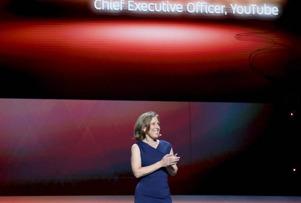 Susan Wojcicki speaking on stage with her name and title displayed on screen behind her.