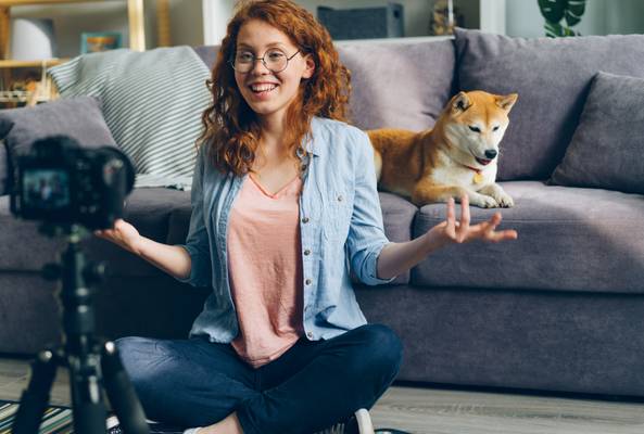 Woman recording video blogging at home with dog lying on couch behind her