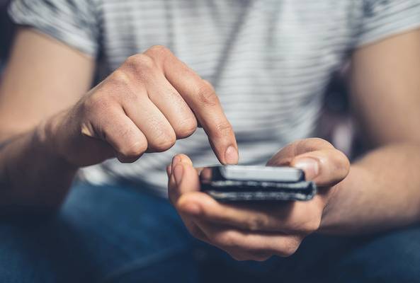 Man using smartphone with finger tapping screen, holding phone in hand close-up