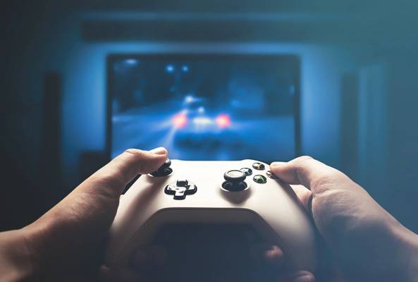 Hands holding a white gaming controller playing a racing game on a TV screen.