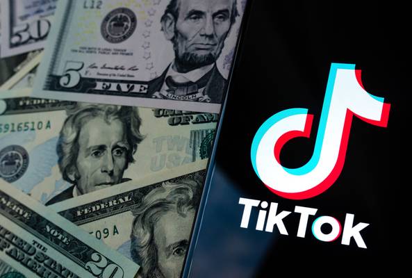 TikTok logo on smartphone screen next to scattered US dollar bills representing revenue.