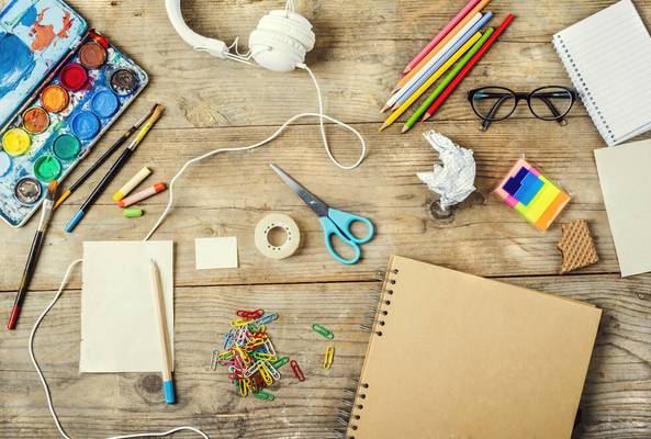 Flat lay of art supplies, stationery, and headphones on wooden desk background.