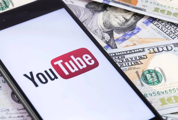 Smartphone displaying YouTube logo overlaid on US hundred dollar bills representing earning.