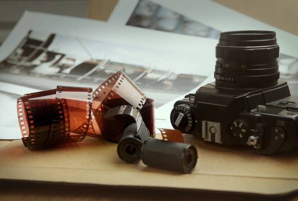 Close-up of vintage film camera with unrolled 35mm photo film and photo prints on table