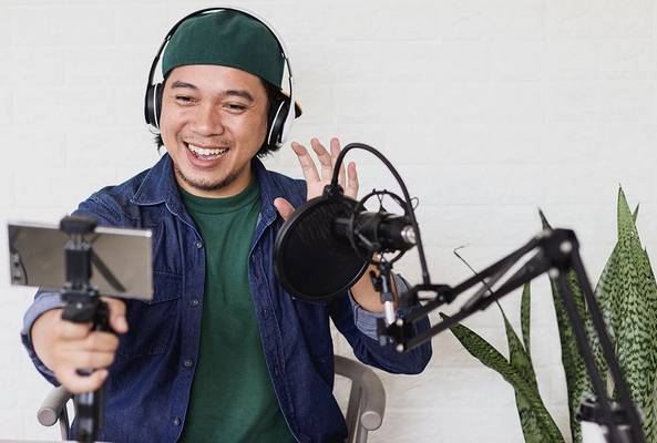 Man wearing headphones recording video podcast with smartphone and microphone at home.