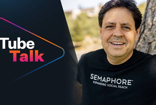 Man smiling outdoors wearing Semaphore social reach t-shirt beside Tube Talk logo graphic