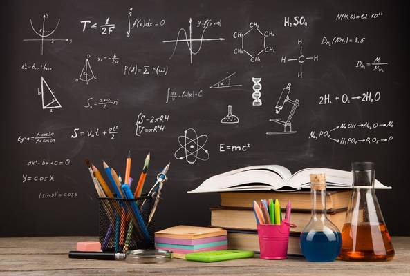 Classroom desk with books, pencils, beakers, and math and chemistry formulas on chalkboard