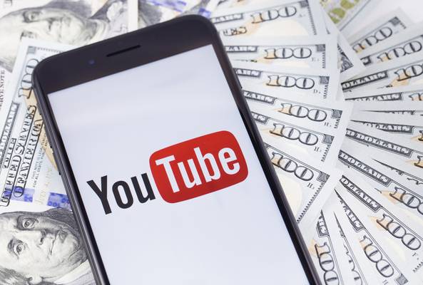 Smartphone displaying YouTube logo on screen over scattered hundred dollar bills.