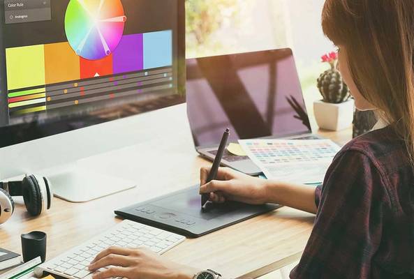 Graphic designer using a digital drawing tablet and color palette software on a desktop computer.