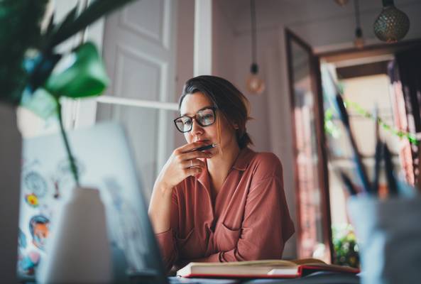 Young woman in glasses working on laptop in cozy home office with natural light