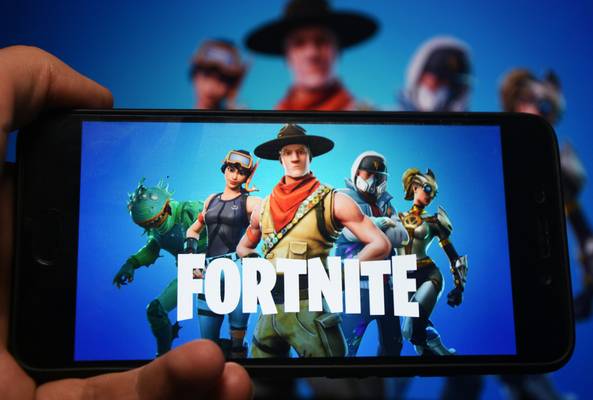 Hand holding smartphone showing Fortnite game characters and logo on screen.