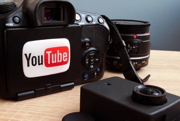 Digital camera with YouTube sticker and additional camera lens on wooden surface