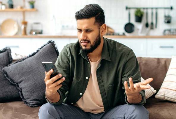 Frustrated man sitting on couch, confused by something on his smartphone screen.