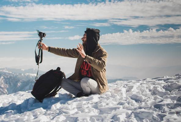Man in winter clothes taking a selfie with a camera on snowy mountain landscape outdoors