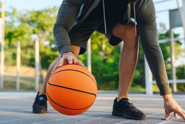 Close-up of a person dribbling an orange basketball on an outdoor court at sunset