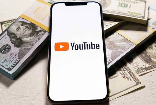 Smartphone displaying YouTube logo on screen with stacks of US hundred-dollar bills.