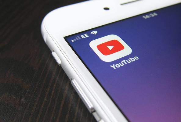 Close-up of white smartphone screen displaying YouTube app icon on wooden surface.