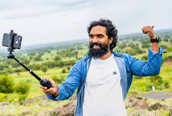 Man with beard taking selfie with smartphone on selfie stick in outdoor nature setting